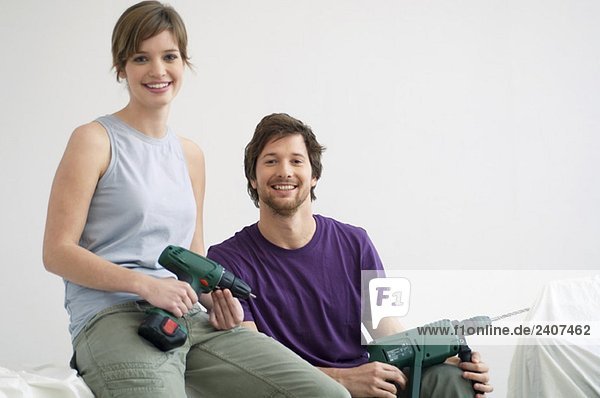Portrait of a mid adult man and a young woman holding drills