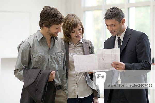 Immobilienmakler  der einem Paar einen Plan zeigt.