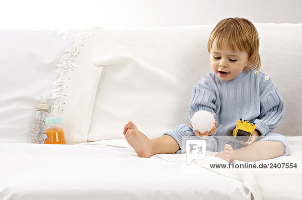 Baby Junge sitzt auf einer Couch und spielt mit Spielzeug