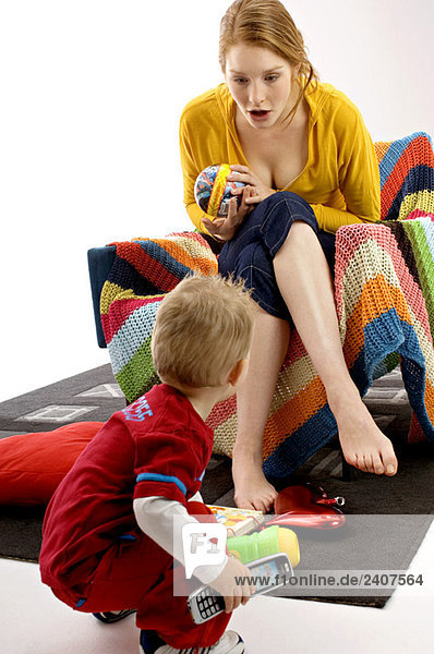 Junge Frau sitzt auf einer Couch und spielt mit ihrem Sohn.
