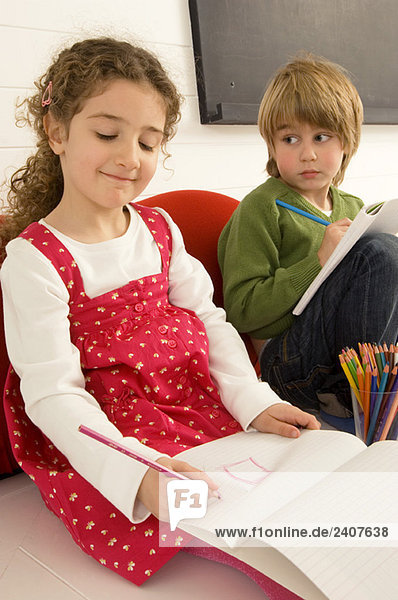 Mädchen malt auf einem Notizblock und ihr Bruder schaut sie an.