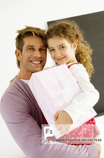 Porträt eines erwachsenen Mannes  der seine Tochter mit einem Geschenk trägt.