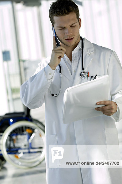 Male doctor reading a medical record and talking on a mobile phone