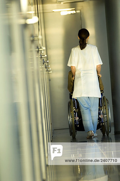 Rückansicht einer Ärztin  die eine Patientin im Rollstuhl schiebt.