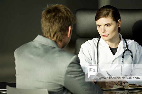 Ärztin am Schreibtisch mit einem männlichen Patienten in der Praxis