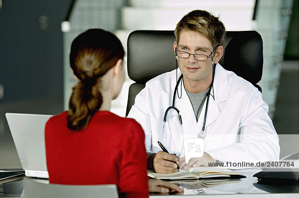 Männlicher Arzt im Gespräch mit einer Patientin in seiner Praxis