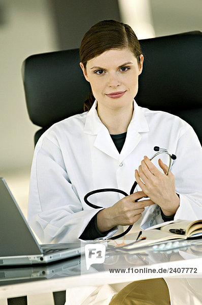 Portrait of a female doctor sitting at a desk and holding a stethoscope in her office