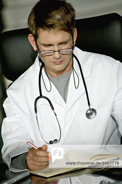 Nahaufnahme eines männlichen Arztes  der am Schreibtisch sitzt und ein Notizbuch liest.