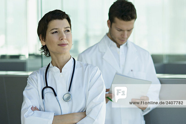 Eine Ärztin steht mit einem Arzt  der medizinische Unterlagen hinter sich hat.