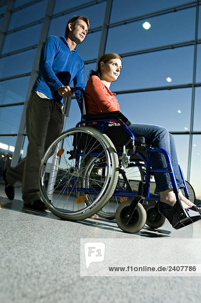 Seitenprofil eines mittelgroßen Mannes  der eine junge Frau im Rollstuhl schiebt.