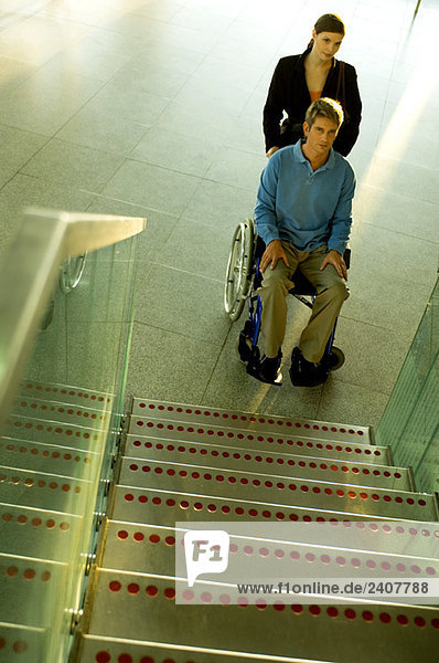Männlicher Patient im Rollstuhl und eine erwachsene Frau neben ihm in der Nähe einer Treppe