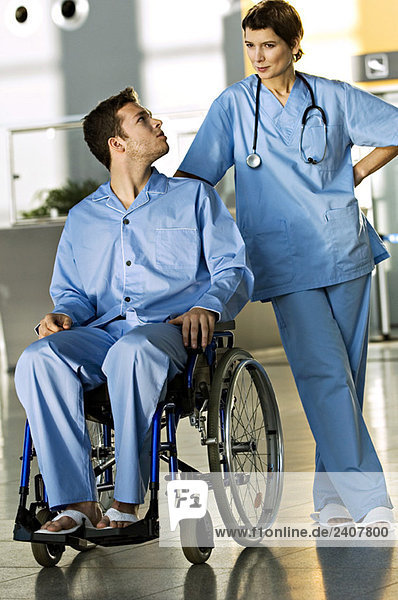 Ein Patient sitzt im Rollstuhl und schaut auf eine Ärztin  die neben ihm steht.