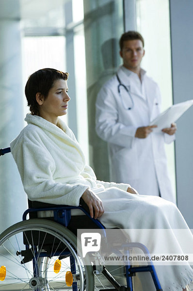 Patientin im Rollstuhl und Arzt im Hintergrund