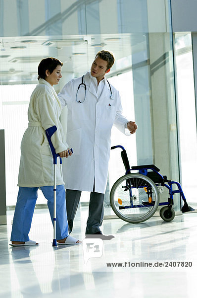 Male doctor assisting a female patient in walking on crutches