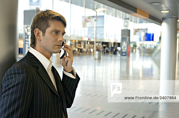 Seitenprofil eines Geschäftsmannes  der auf einem Handy am Flughafen spricht