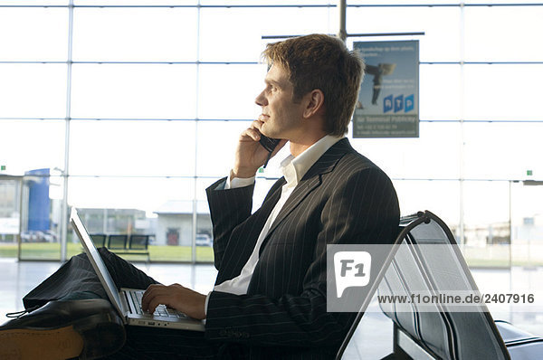 Seitenprofil eines Geschäftsmannes mit Laptop und Handy in einer Flughafenlounge