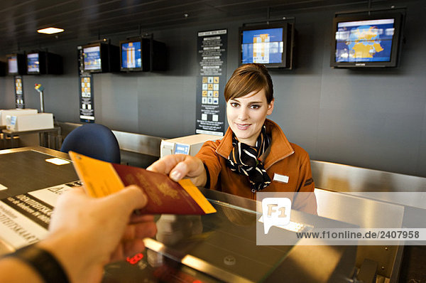 Flugbegleiterin  die einem Fluggast einen Reisepass und eine Bordkarte gibt.