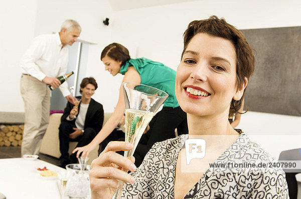 Mittlere erwachsene Frau hält ein Weinglas mit drei Personen im Hintergrund.