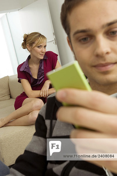 Nahaufnahme eines jungen Mannes mit einem MP3-Player  hinter dem eine junge Frau sitzt.