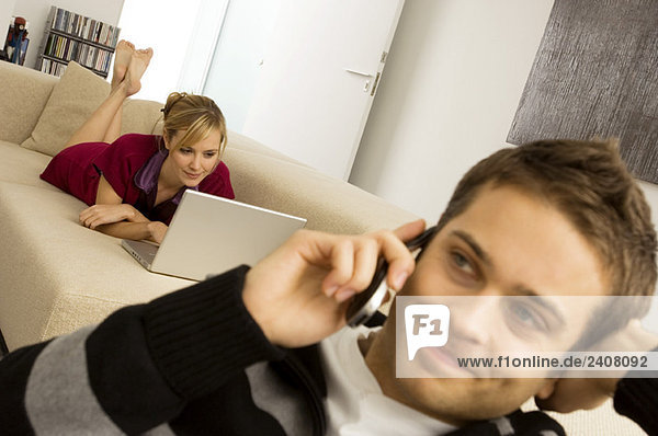 Junger Mann mit Handy und junge Frau mit Laptop im Hintergrund