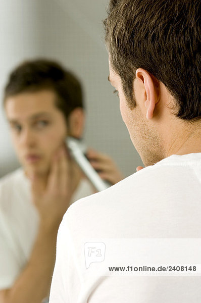 Rückansicht eines jungen Mannes  der sich mit einem elektrischen Rasierapparat rasiert.