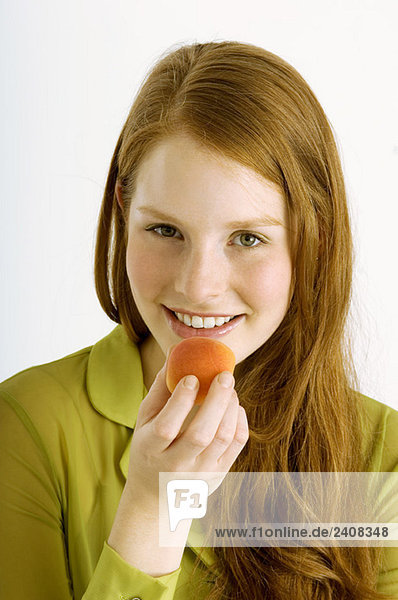 Porträt einer jungen Frau  die eine Aprikose isst und lächelt