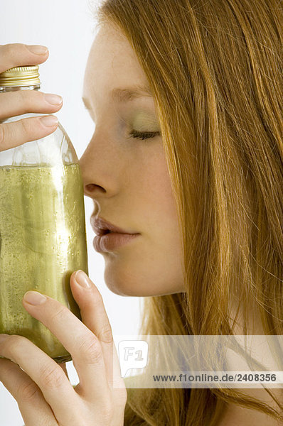 Nahaufnahme einer jungen Frau  die eine Flasche Aromatherapieöl riecht.