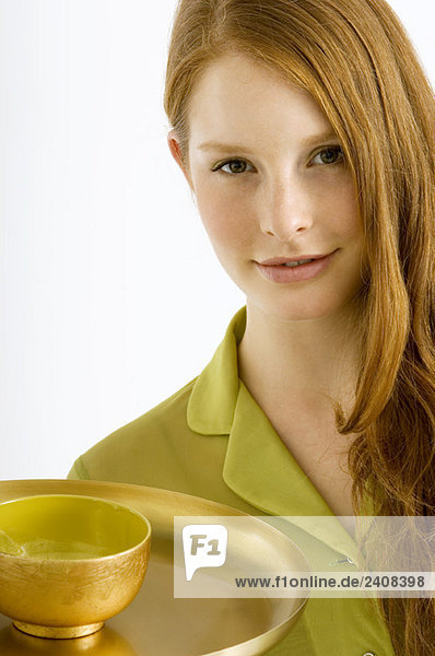 Porträt einer jungen Frau  die eine Schale mit Massageöl auf einem Teller hält.