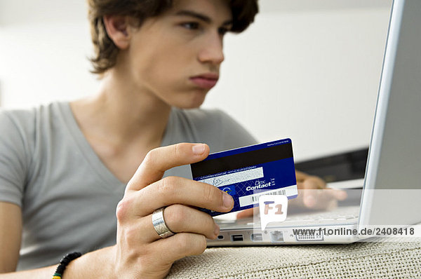Close-up of a teenage boy using a laptop and holding a credit card