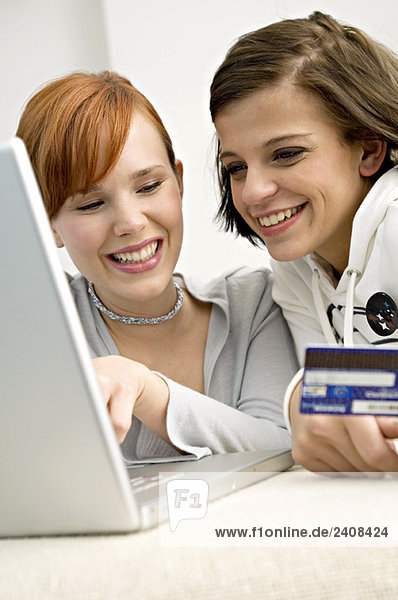Nahaufnahme von zwei jungen Frauen  die eine Kreditkarte besitzen und einen Laptop benutzen.