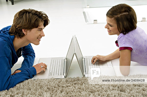 Seitenprofil einer jungen Frau und eines Teenagers  die sich gegenseitig anschauen und Laptops benutzen.