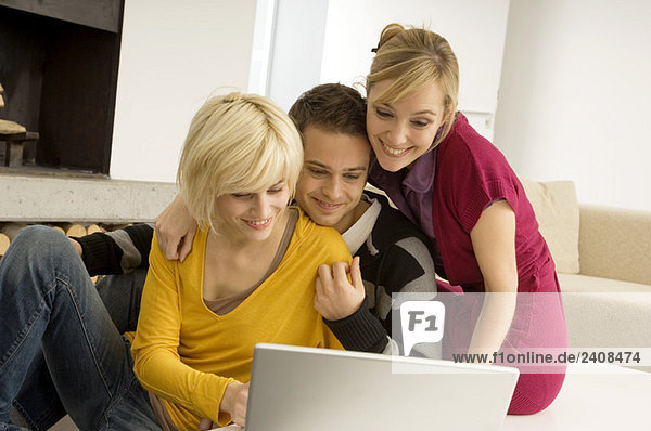 Junger Mann mit zwei jungen Frauen  die auf einen Laptop schauen und lächeln.