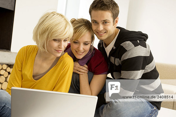 Zwei junge Frauen und ein junger Mann sitzen vor einem Laptop und lächeln