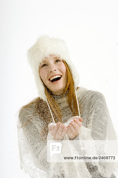 Junge Frau hält Schnee in ihren hohlen Händen und lächelt