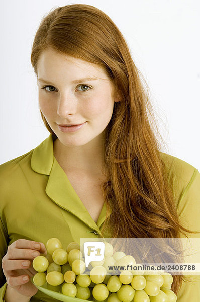 Porträt einer jungen Frau  die einen Teller Weintrauben hält und lächelt.