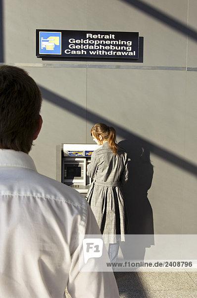 Rear view of a businessman looking at a businesswoman using an ATM
