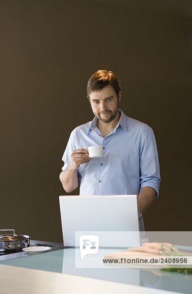 Ein Mann  der einen Laptop benutzt und eine Kaffeetasse hält.