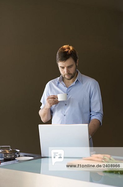 Ein Mann  der einen Laptop benutzt und eine Kaffeetasse hält.