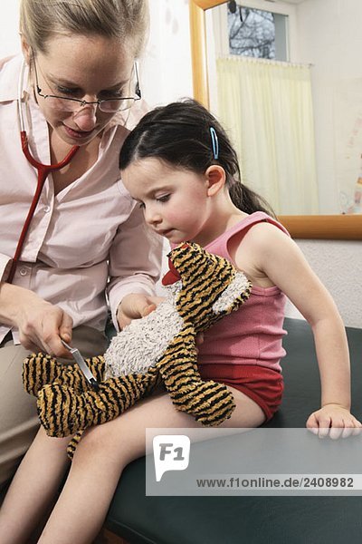 A doctor checking the reflexes of a young girl’s stuffed animal