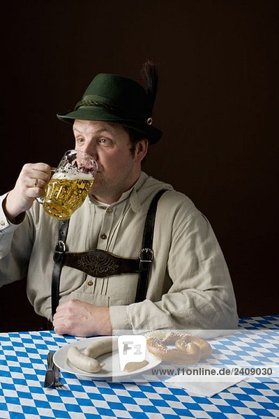 Stereotypischer deutscher Mann in bayerischer Tracht bei Bier und deutschem Essen
