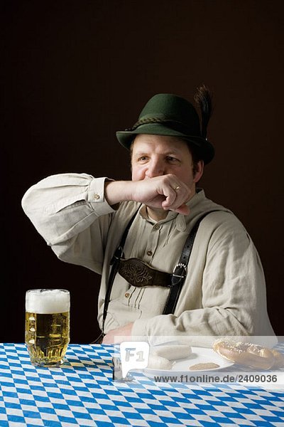 Stereotypischer deutscher Mann in bayerischer Tracht  der mit Bier und deutschem Essen den Mund wischt.