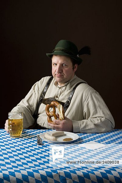 Stereotypischer deutscher Mann in bayerischer Tracht  der mit Bier und deutschem Essen den Mund wischt.