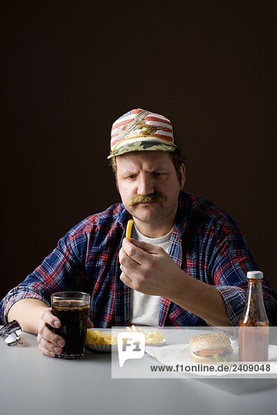 Ein stereotyper Amerikaner  der eine Pommes frites hält und sie anstarrt.