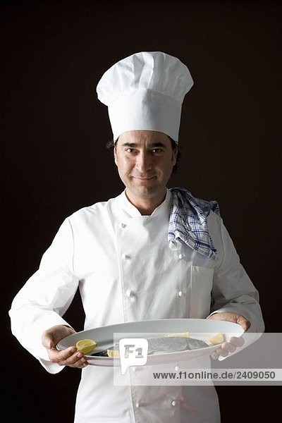 Stereotypischer Koch posiert mit einer Fischplatte