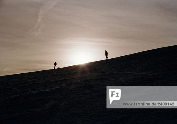 Two skiers on a mountain side at sunset