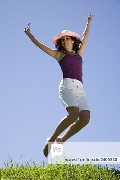 Eine junge Frau  die in die Luft springt und ein Handy hält.