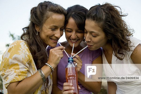 Drei Frauen  die durch Strohhalme aus einer Flasche trinken.