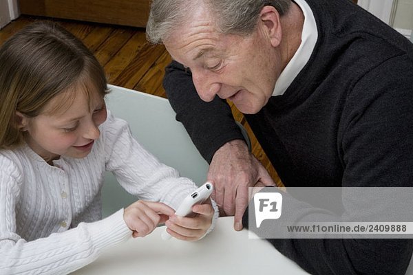 A granddaughter using a electronic device while her grandfather watch