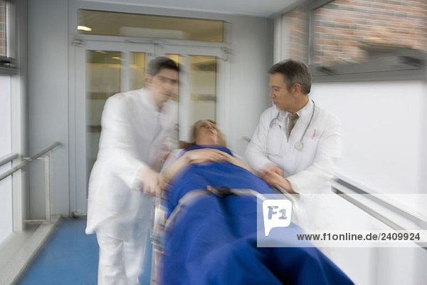 Zwei Mitarbeiter des Gesundheitswesens schieben einen Patienten durch einen Korridor.