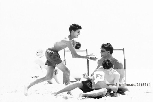 Mann Roughhousing am Strand mit jugendlichen Söhnen  schwarz-weiß